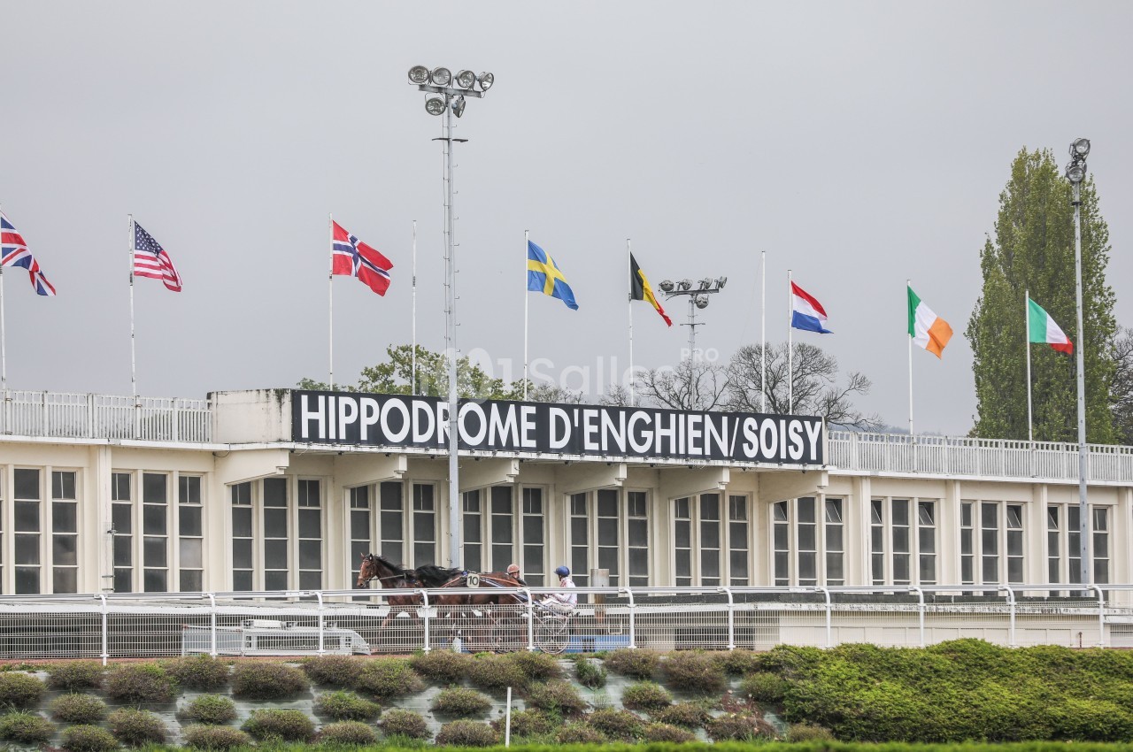 Façade de l'hippodrome d'Enghien-Soisy avec des drapeaux internationaux et un cheval attelé au premier plan.