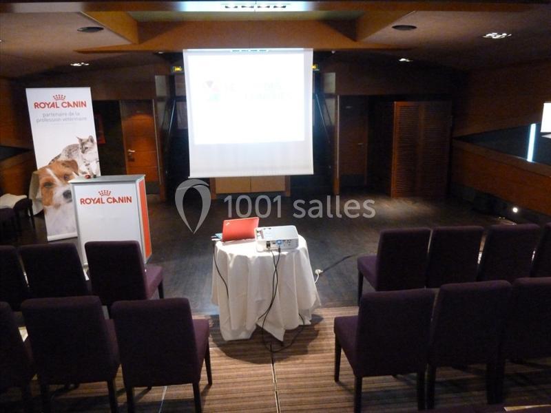 Salle de conférence vide avec des chaises alignées, un projecteur, un écran blanc et des affiches Royal Canin.