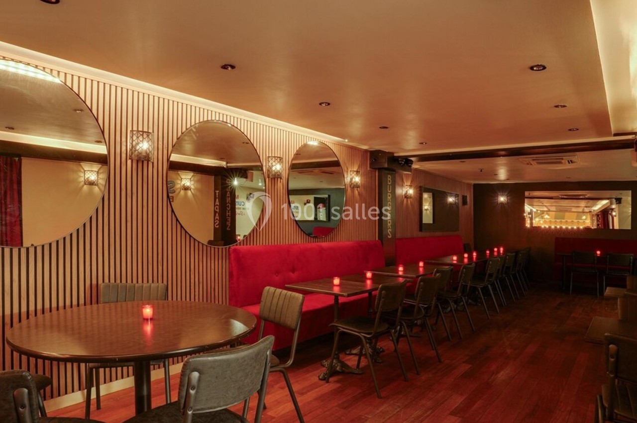 Salle de restaurant chaleureuse avec tables rondes, banquettes rouges, miroirs circulaires et éclairage tamisé.