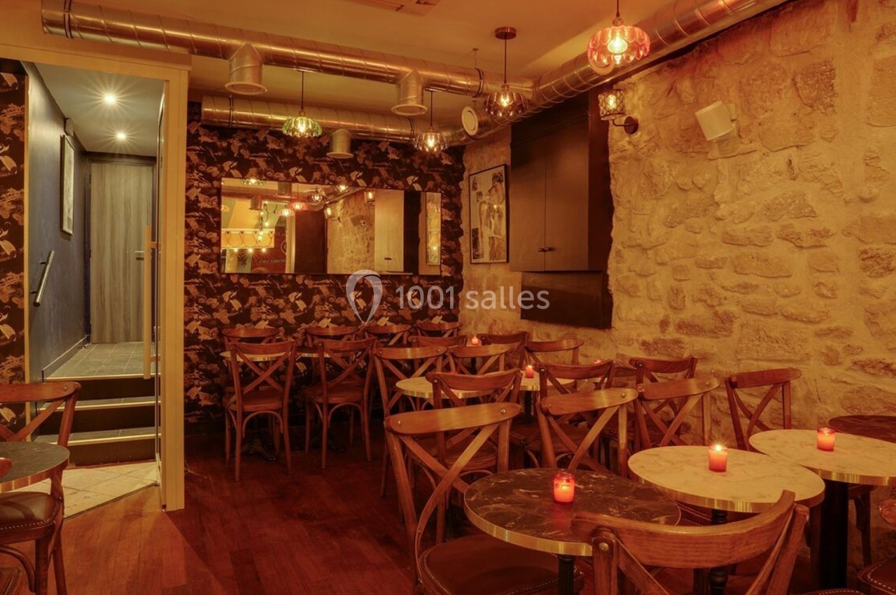 Salle de restaurant chaleureuse avec murs en pierre, tables rondes, chaises en bois et éclairage tamisé.