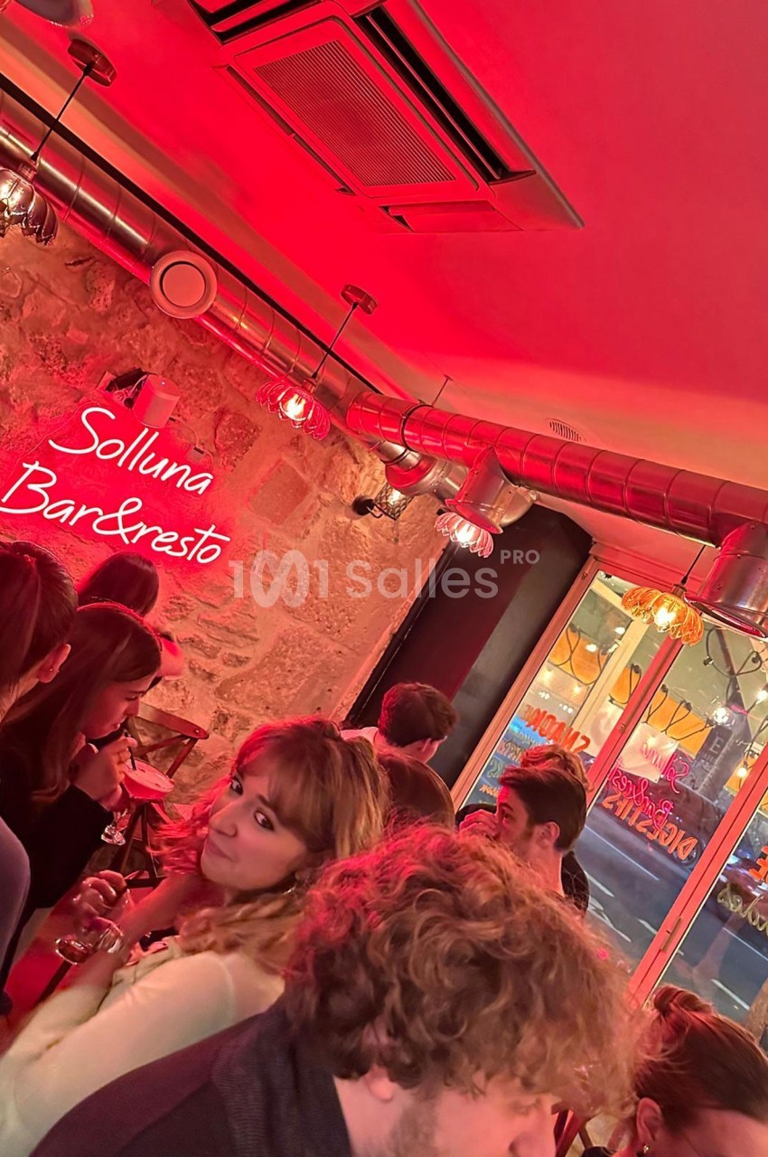 Groupe de personnes dans un bar à l'éclairage rouge, avec une enseigne lumineuse ’Solluna Bar & Resto’ en arrière-plan.