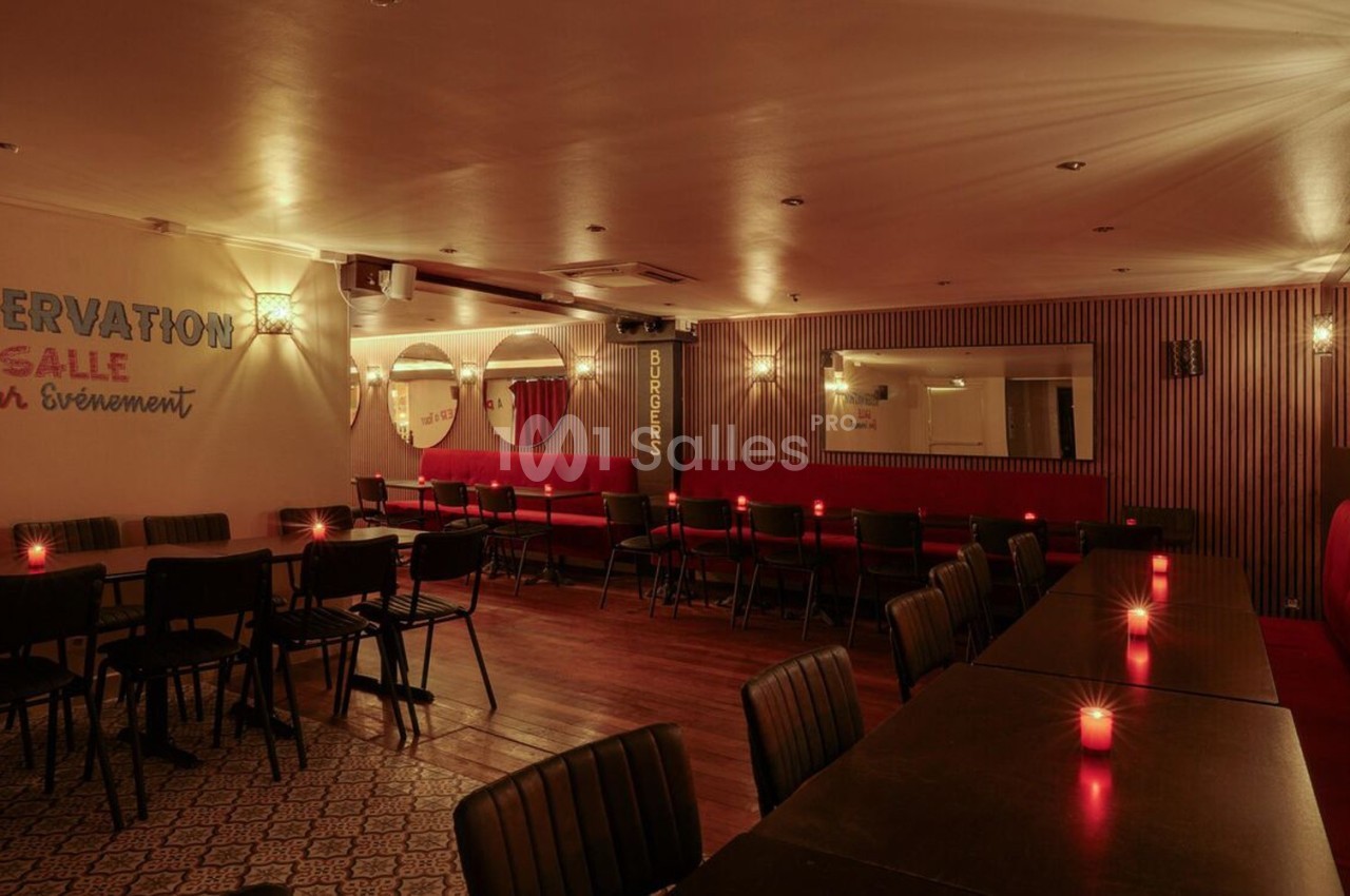 Salle de restaurant éclairée par des bougies, avec des tables noires, des chaises et des banquettes rouges.