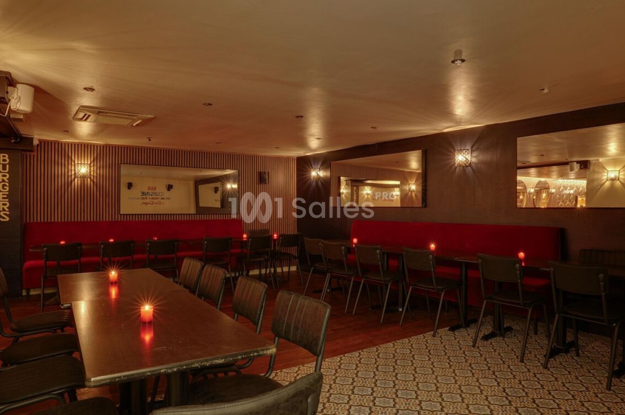 Salle de restaurant avec tables en bois sombre, chaises noires, banquettes rouges et éclairage tamisé.