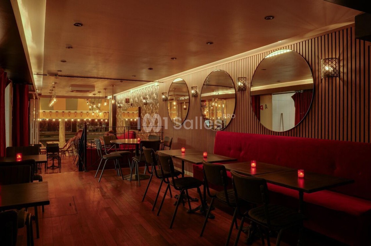 Salle de restaurant chaleureuse avec tables en bois, banquettes rouges, miroirs ronds et éclairage tamisé.