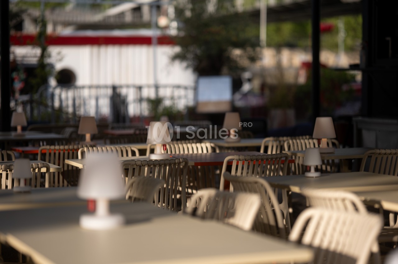 Terrasse d'un café avec des tables et des chaises vides, éclairées par des lampes de table en plein jour.