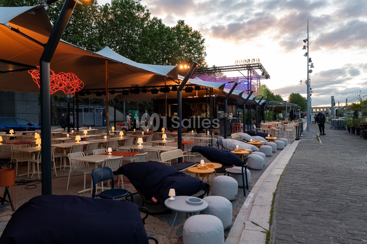 Terrasse extérieure d'un restaurant avec tables, chaises et éclairage, située le long d'une promenade au coucher du soleil.