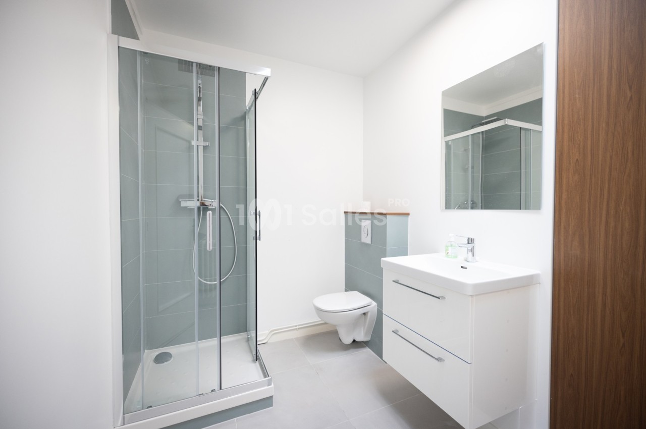 Salle de bain moderne avec douche vitrée, meuble vasque blanc, miroir et toilettes suspendues.