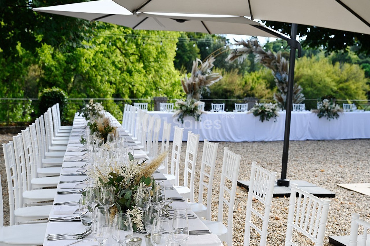 Tables de réception décorées avec des fleurs blanches et pampas, disposées en extérieur sous des parasols.