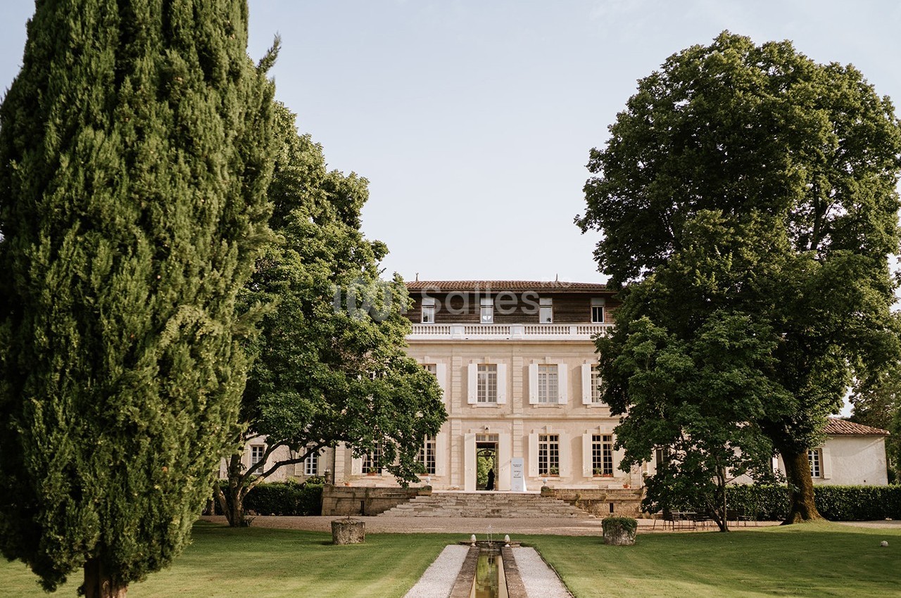 Façade d'un grand bâtiment ancien entouré d'arbres et d'une pelouse bien entretenue, par une journée ensoleillée.