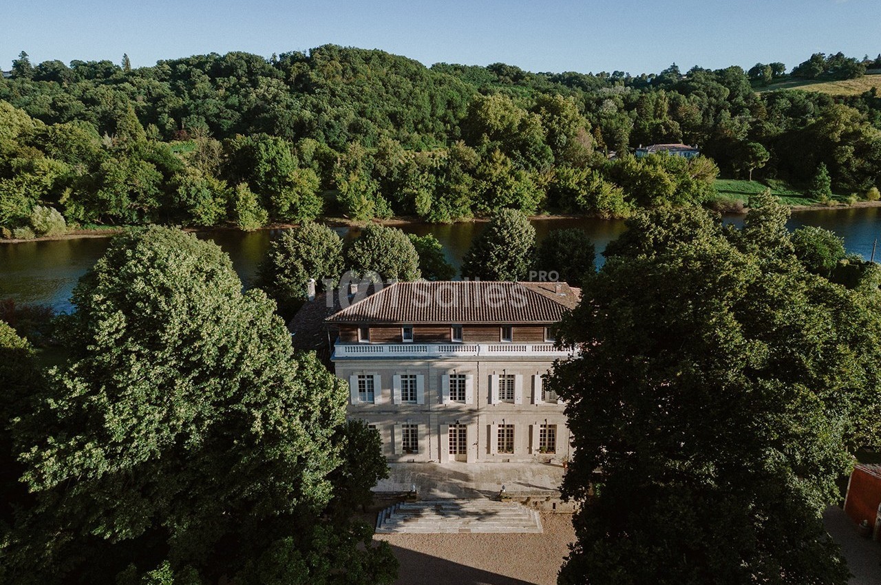 Manoir entouré d'arbres, situé près d'une rivière, sous un ciel dégagé.