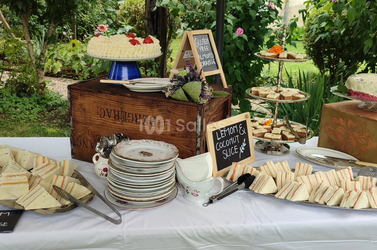 Buffet en plein air avec assiettes de sandwiches, gâteaux, et panneaux indiquant des options sans gluten et végétaliennes.