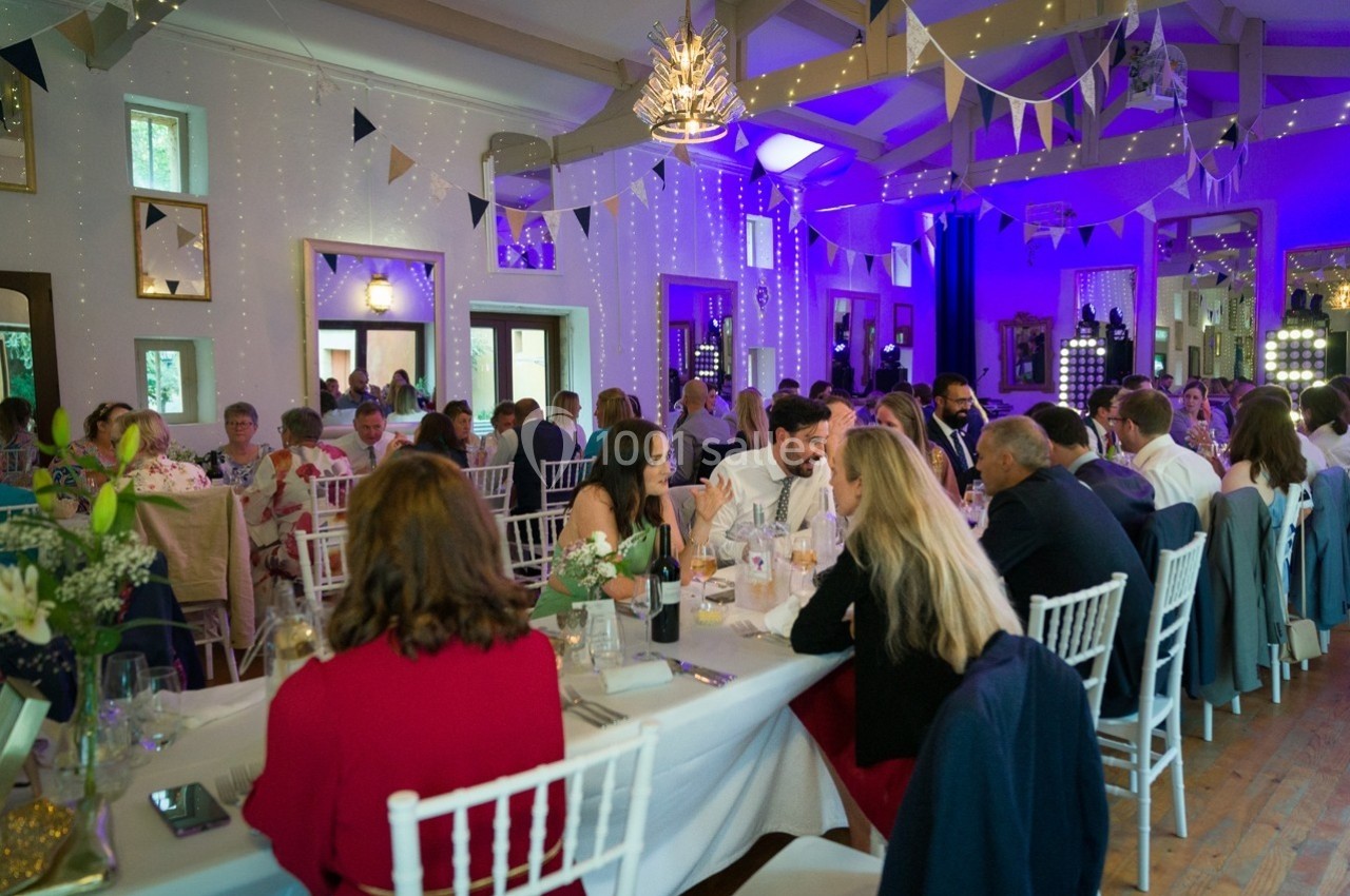 Salle décorée pour un événement, avec des invités assis à des tables, éclairage tamisé et guirlandes suspendues.