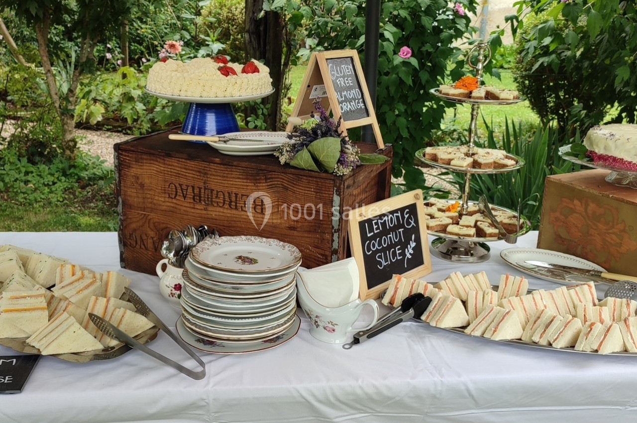Buffet en plein air avec assiettes de sandwiches, gâteaux variés et panneaux indiquant des options sans gluten.