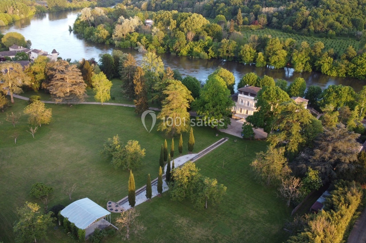 Vue aérienne d'un domaine avec une grande maison entourée d'arbres, près d'une rivière et d'espaces verts.