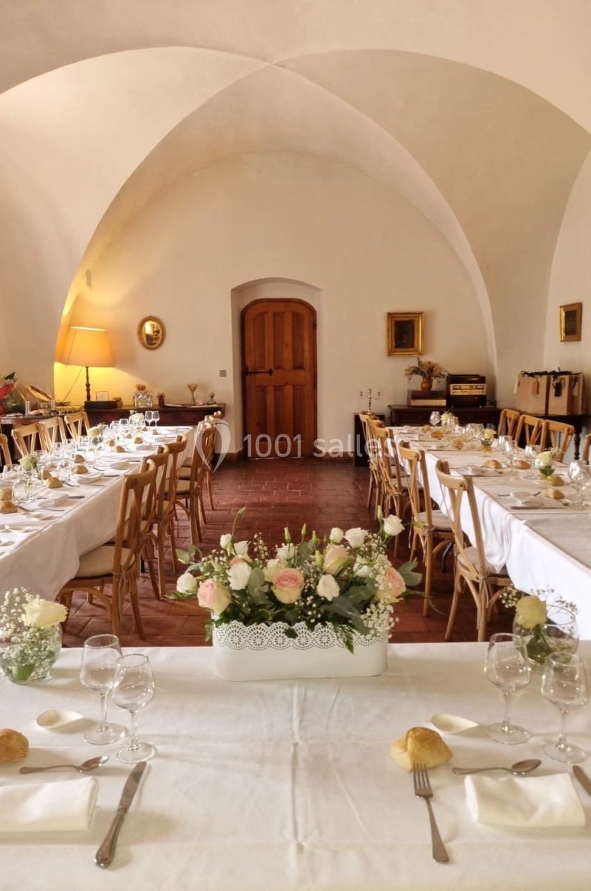 Salle voûtée décorée pour un repas, avec tables dressées, nappes blanches et centre de table floral.