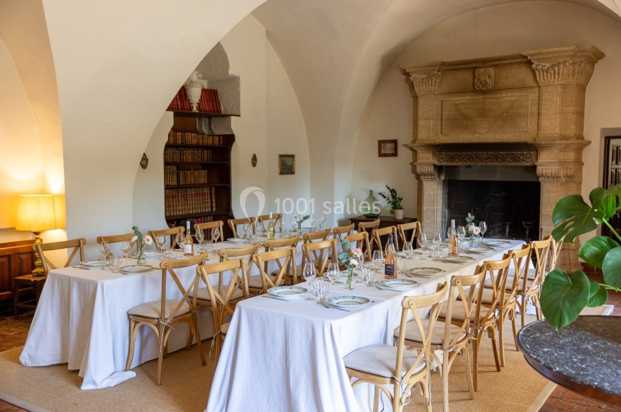 Salle à manger élégante avec deux grandes tables dressées, chaises en bois et cheminée en pierre dans un décor classique.
