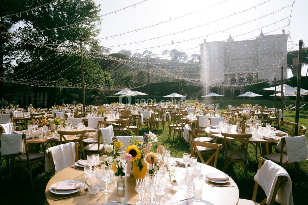 Tables décorées pour un événement en plein air avec guirlandes lumineuses, fleurs et vaisselle élégante.