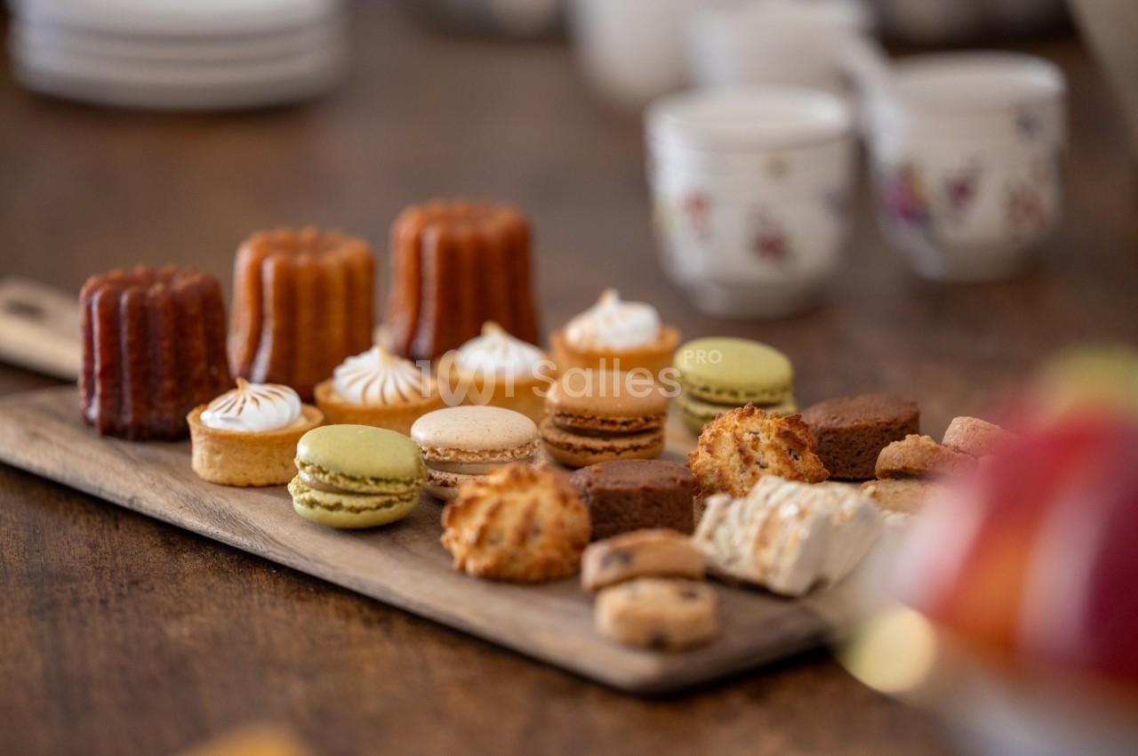 Plateau en bois avec un assortiment de pâtisseries françaises, macarons, cannelés et autres douceurs, sur une table en bois.