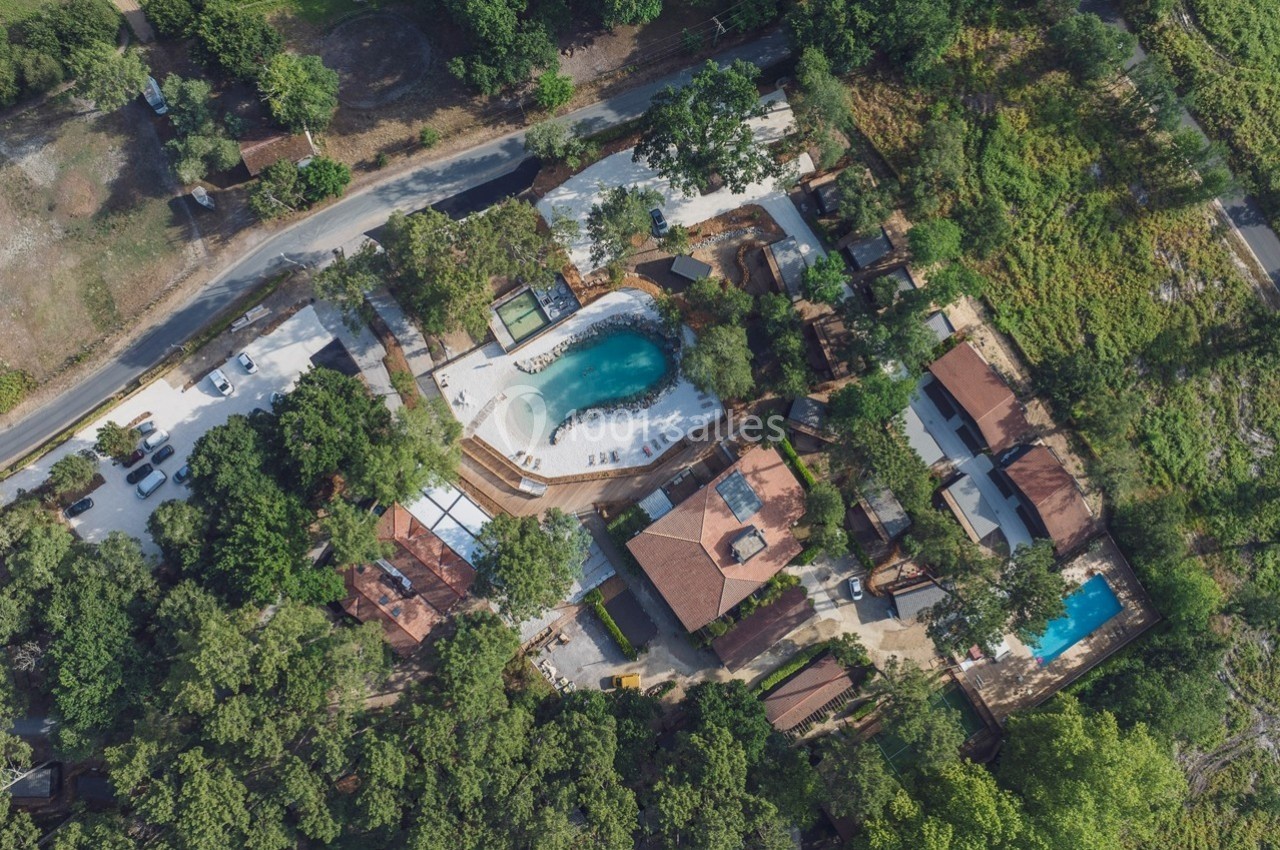 Vue aérienne d'un complexe avec piscine, bâtiments et espaces verts entourés de végétation dense.
