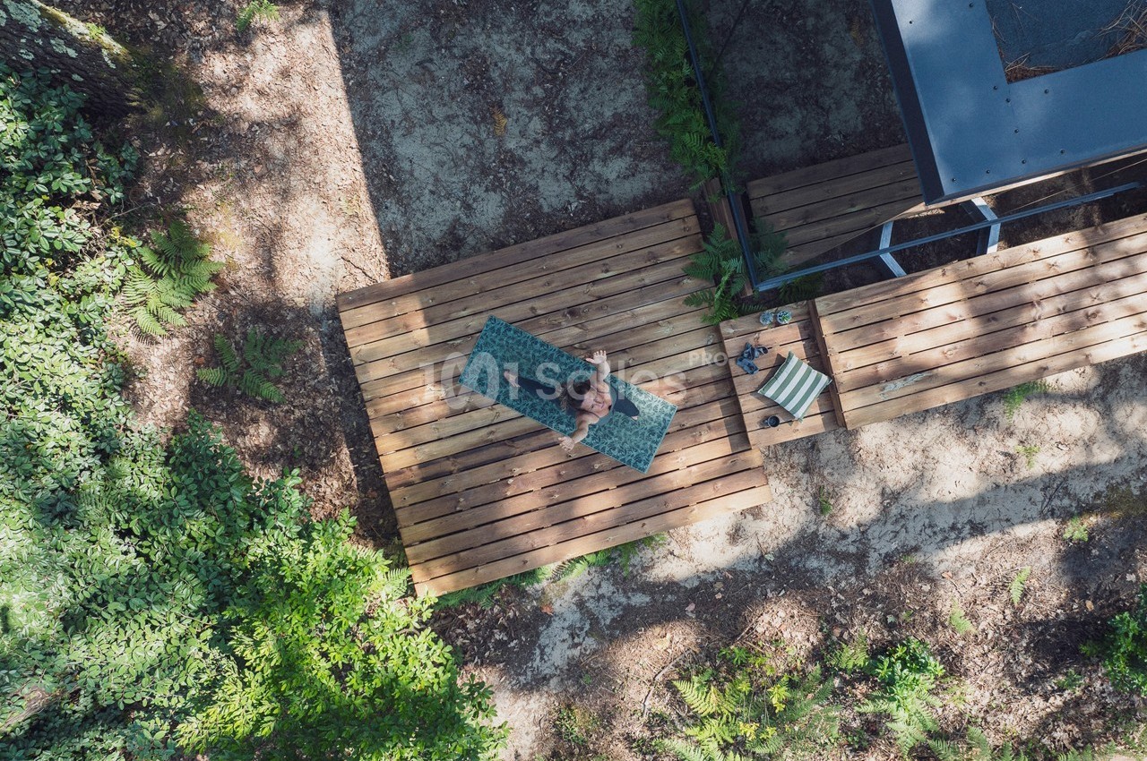 Vue aérienne d'une personne assise sur une terrasse en bois entourée de végétation.