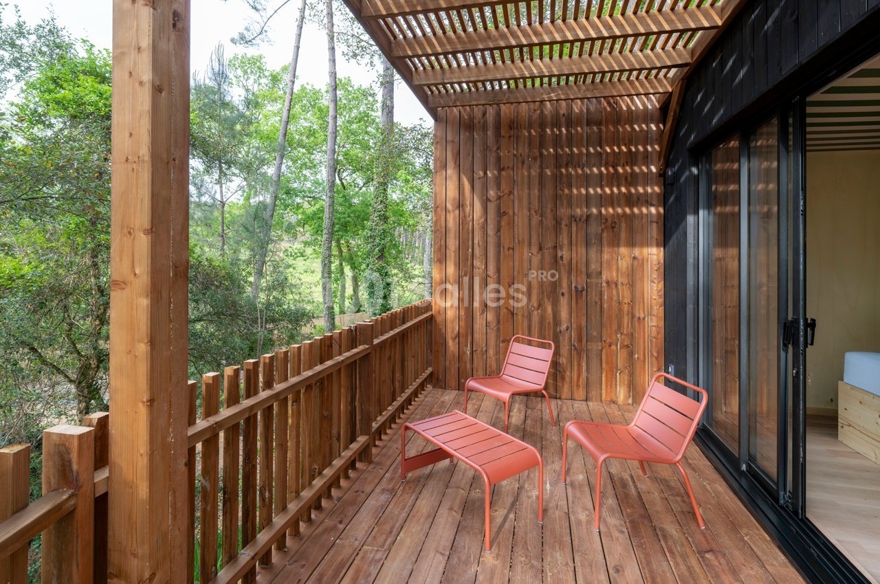 Terrasse en bois avec trois chaises rouges, entourée de verdure et partiellement ombragée par une pergola.
