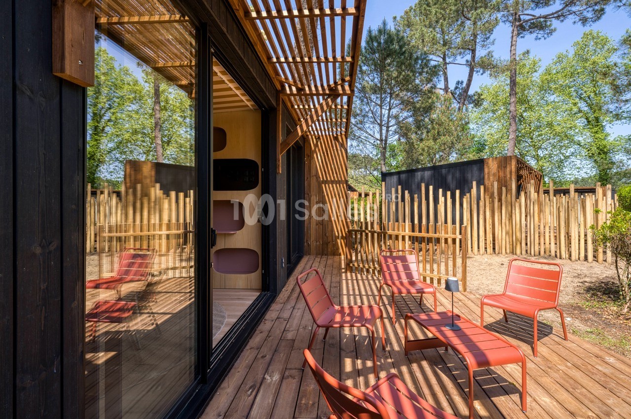 Terrasse en bois avec mobilier rouge, entourée de palissades en bois et de végétation sous un ciel dégagé.
