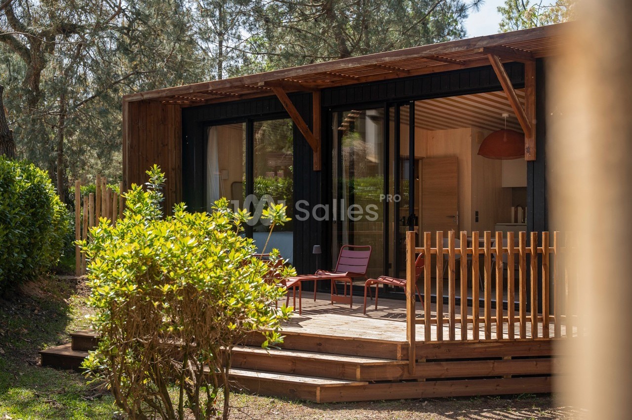Terrasse en bois avec fauteuils devant une maison moderne entourée de végétation et de pins.