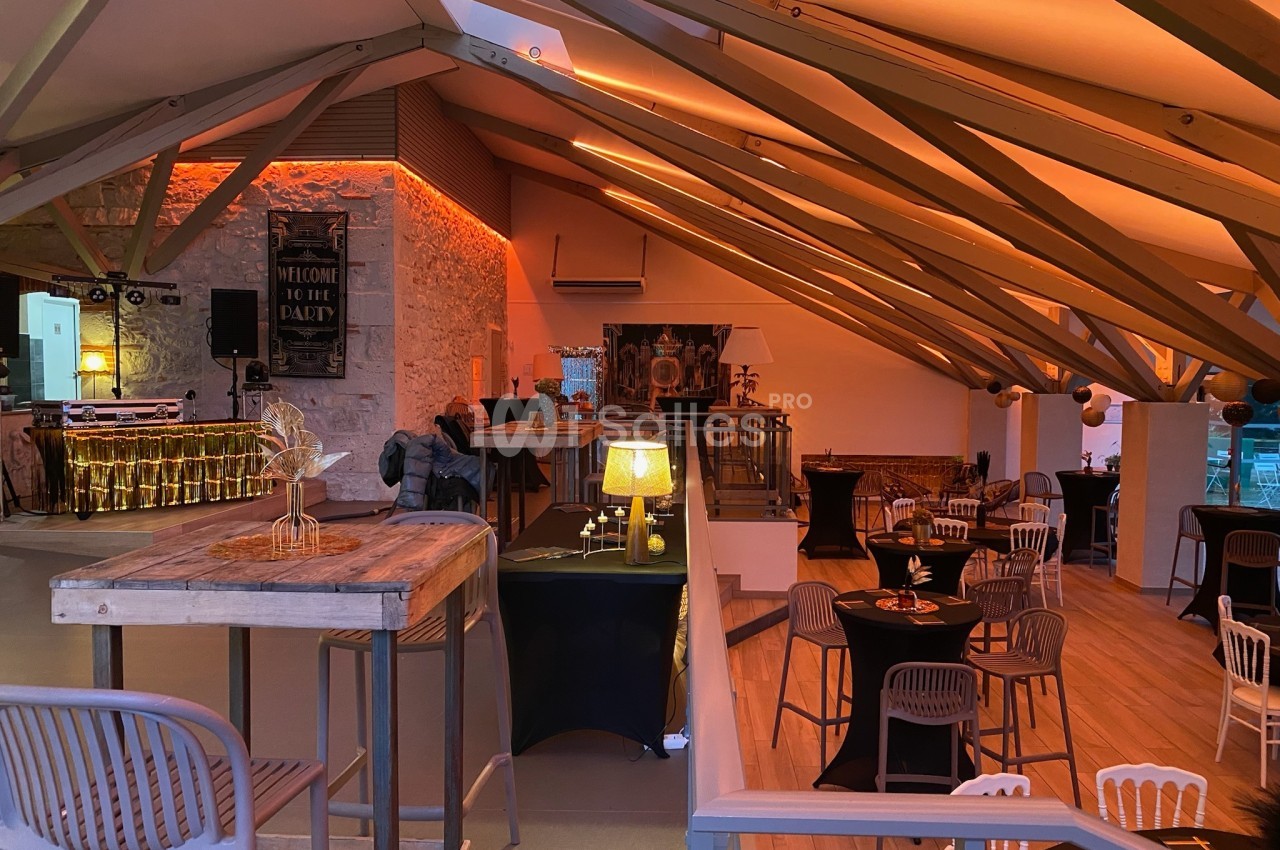 Salle de réception décorée avec des tables hautes et basses, éclairage chaleureux et ambiance festive.