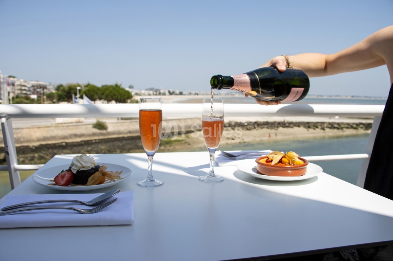 Terrasse avec vue sur l'estuaire, table dressée avec flûtes de champagne rosé, assiettes et verres d'eau.
