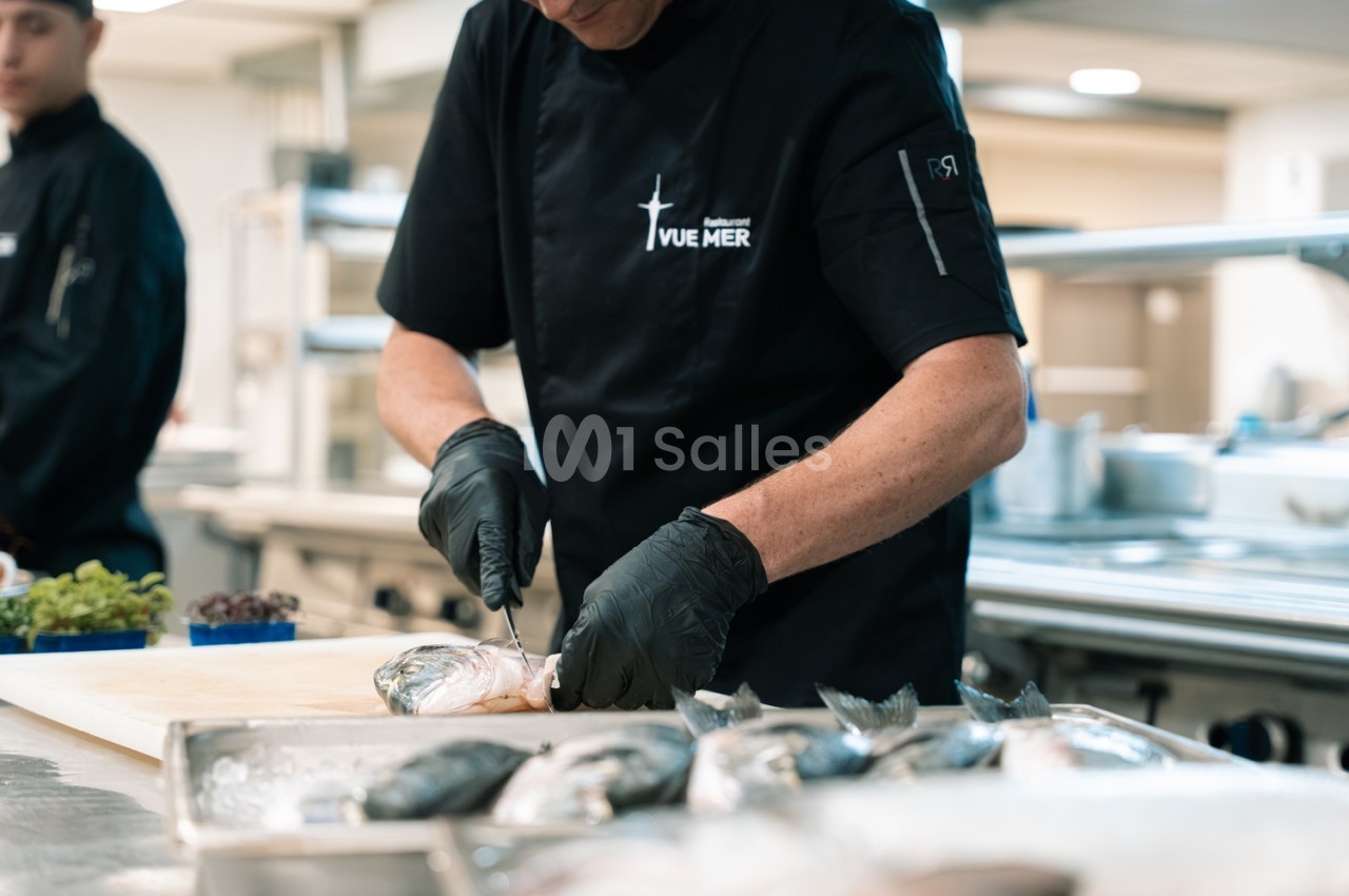 Cuisinier en tenue noire prépare du poisson à la cuisine - intérieur moderne et bien éclairé.