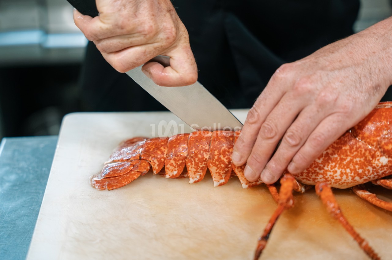 Chef découpant un homard cuit à la chair blanche et rouge sur planche à découper.