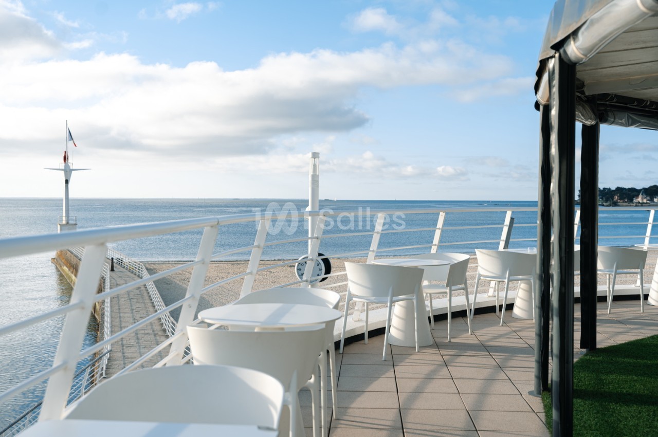Terrasse aérée avec tables et chaises blanches face à la mer et plage de sable fin.