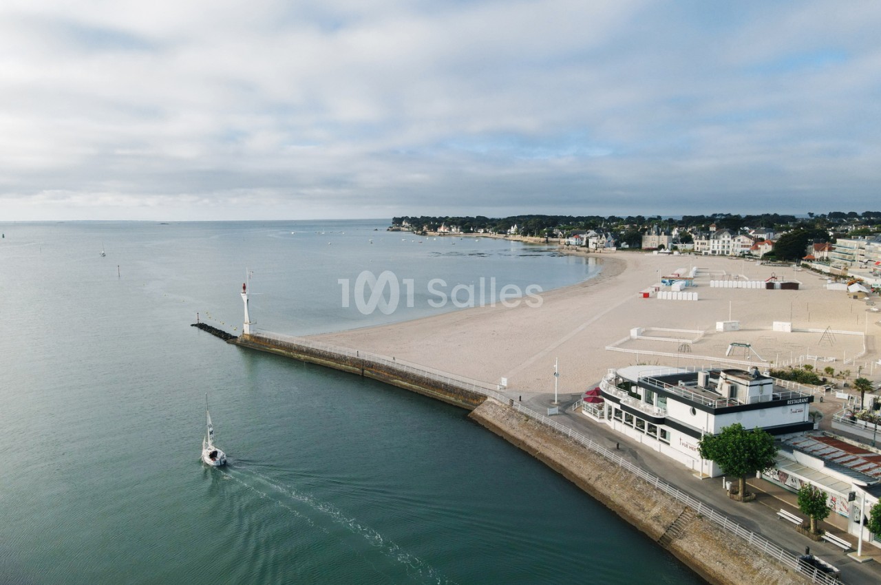 Plage de sable avec jetée, bateau blanc amarré et bâtiment blanc en bordure côtière - vue depuis le restaurant.