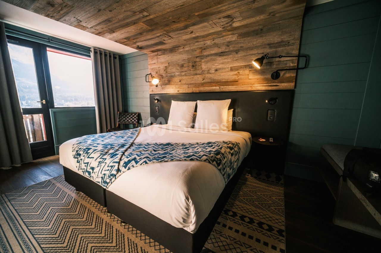 Chambre avec lit double, tête de lit en bois, éclairage mural, grande fenêtre et décoration moderne.