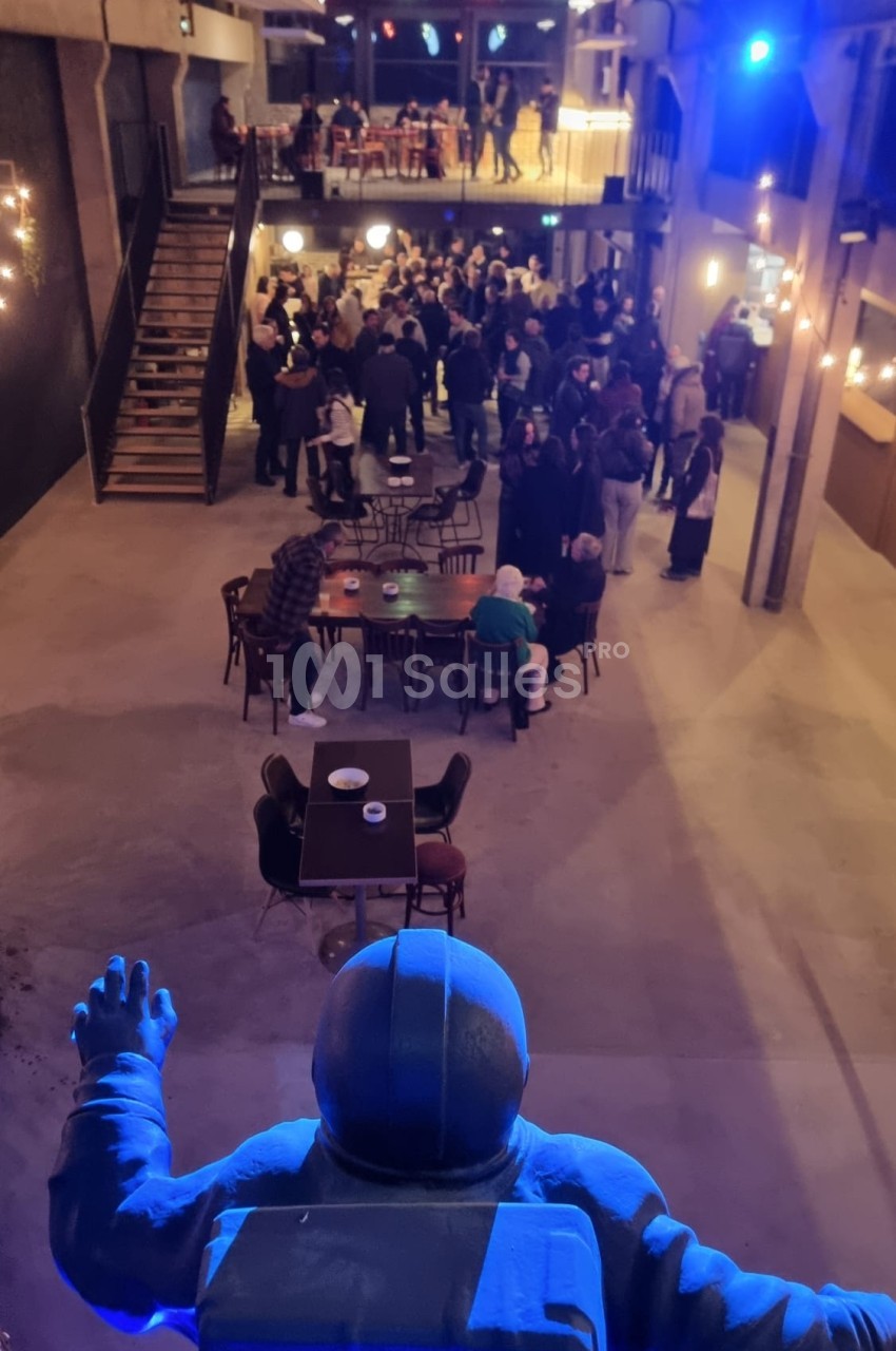 Vue d'une salle animée avec des groupes de personnes debout et assises, observée depuis une statue d'astronaute.