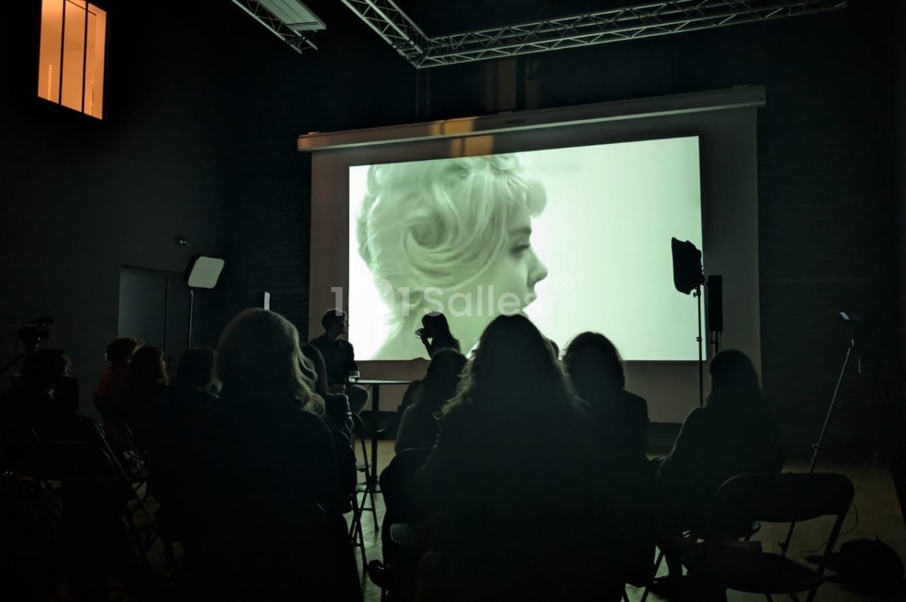 Projection d'un film en noir et blanc dans une salle sombre, avec des spectateurs assis devant l'écran.