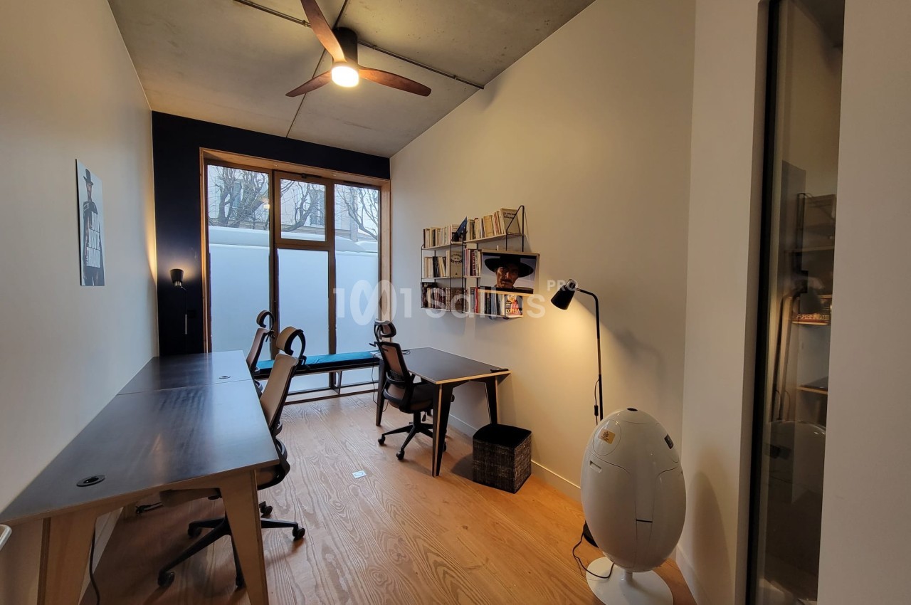 Bureau moderne avec deux postes de travail, étagères murales, lampe sur pied et grande fenêtre laissant entrer la lumière…