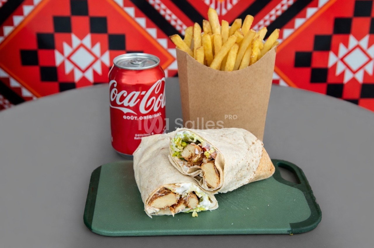 Un wrap garni de légumes et poulet, accompagné de frites et d'une canette de soda sur une planche verte.