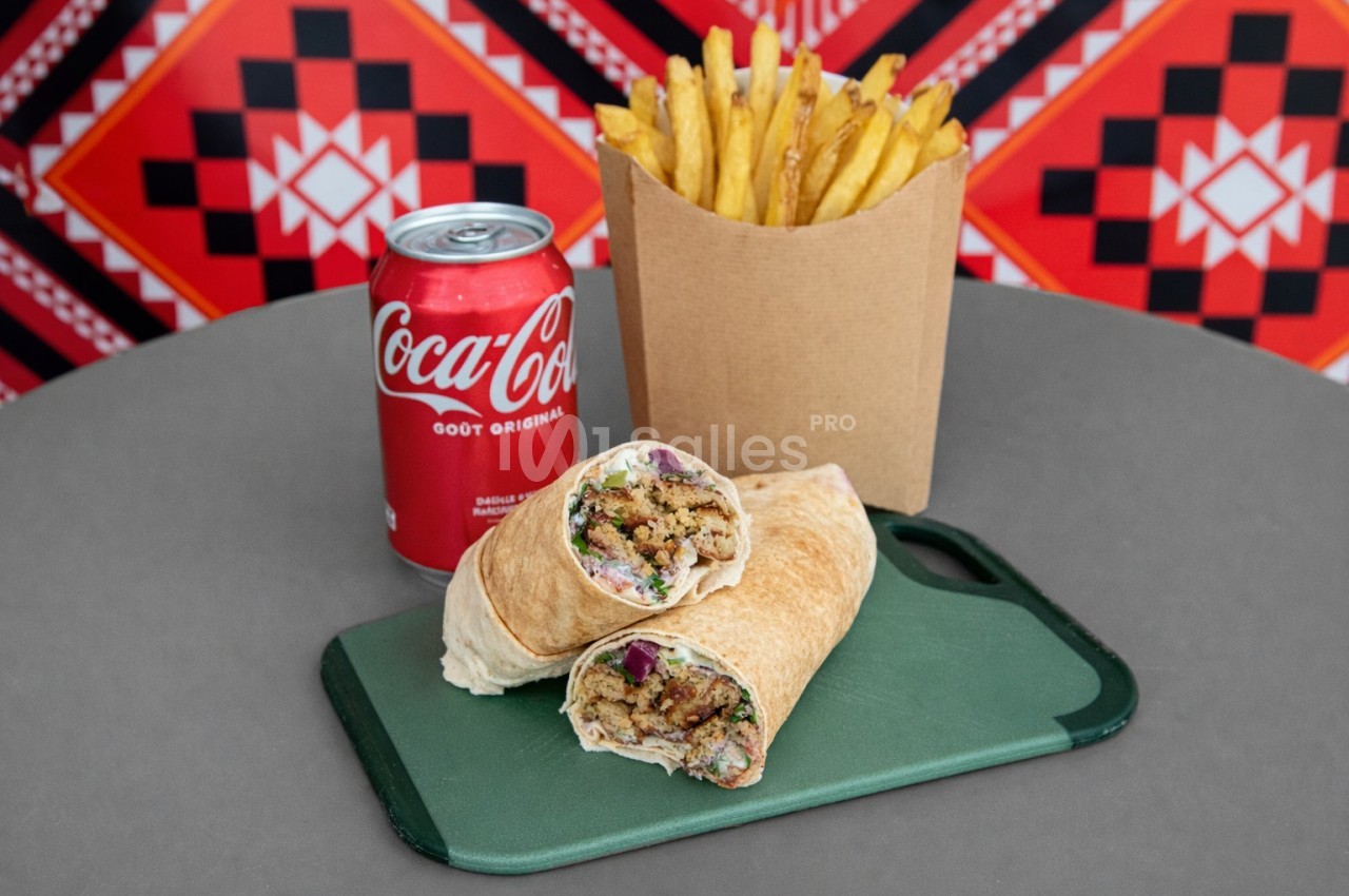 Un wrap garni coupé en deux, accompagné de frites et d'une canette de soda, sur une table grise.