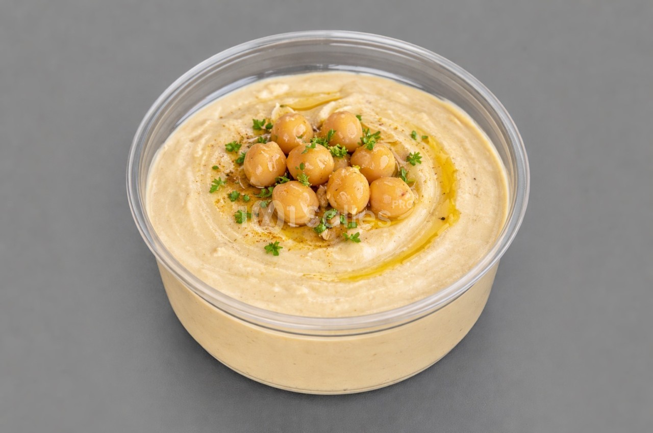 Bol de houmous garni de pois chiches, persil et filet d'huile d'olive, sur fond gris.