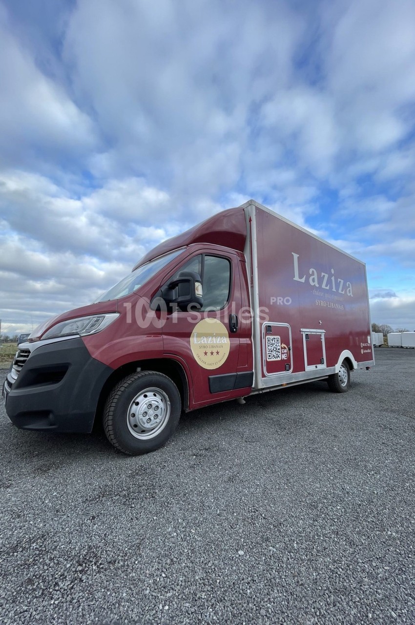 Camion rouge stationné sur un sol gravillonné, avec le logo ’Laziza’ visible sur sa carrosserie.