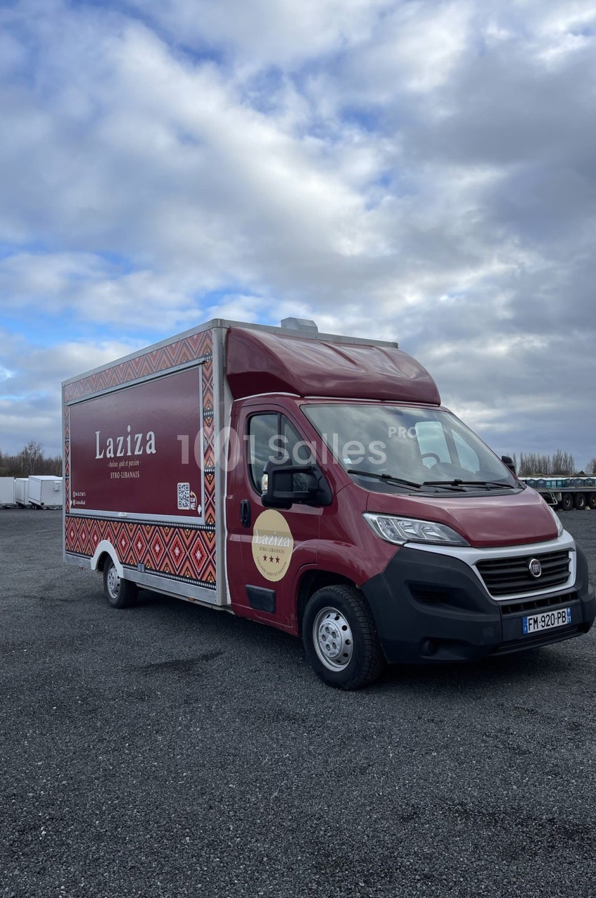 Camion rouge Laziza stationné sur un parking, avec un ciel nuageux en arrière-plan.