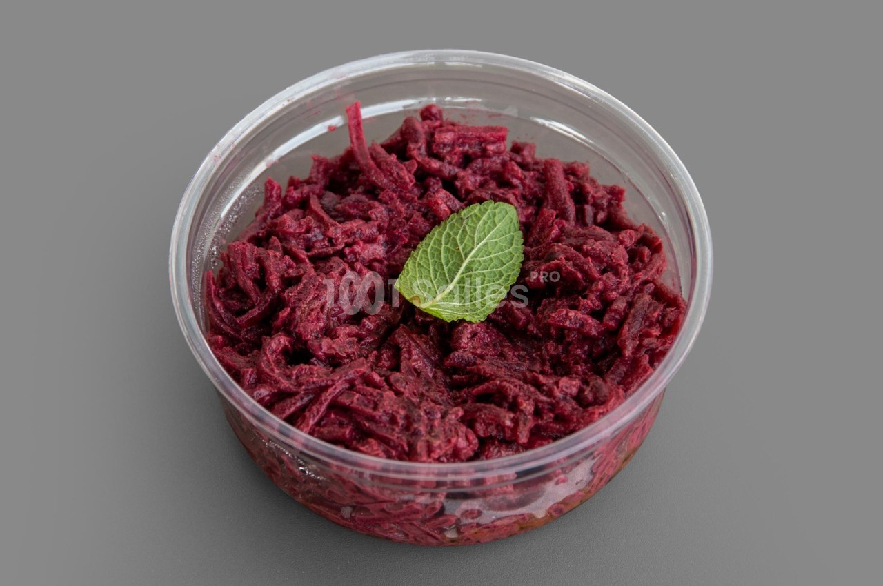 Salade de betteraves râpées dans un récipient transparent, garnie d'une feuille de menthe sur un fond gris.