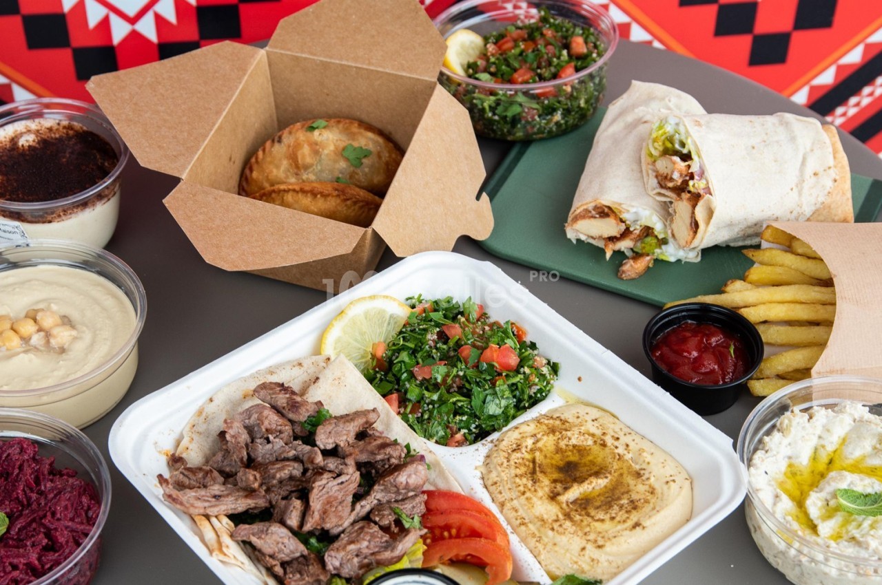 Assortiment de plats méditerranéens avec viandes grillées, houmous, taboulé, wraps, frites et desserts.