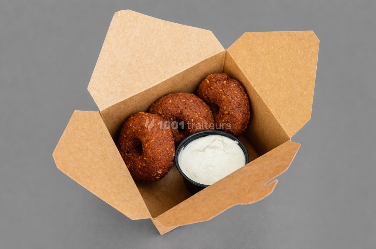 Trois falafels dans une boîte en carton avec un petit récipient de sauce blanche.