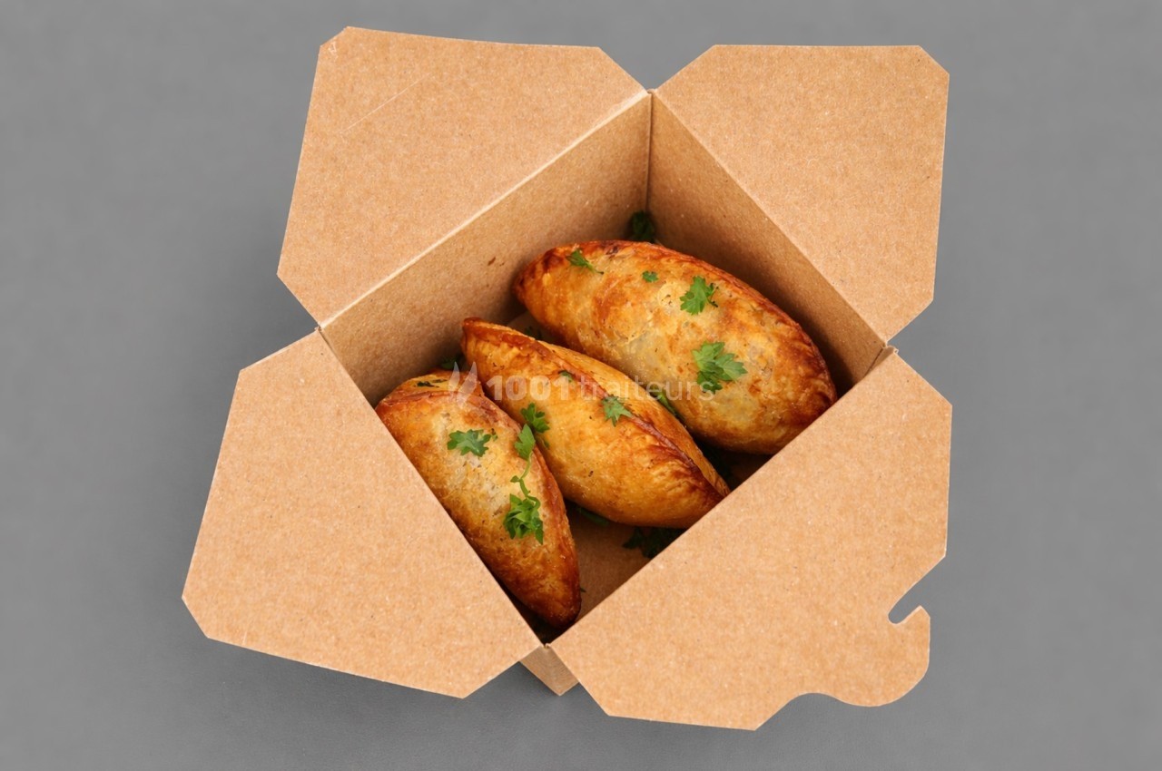 Trois empanadas dorées garnies de persil dans une boîte en carton ouverte sur un fond gris.