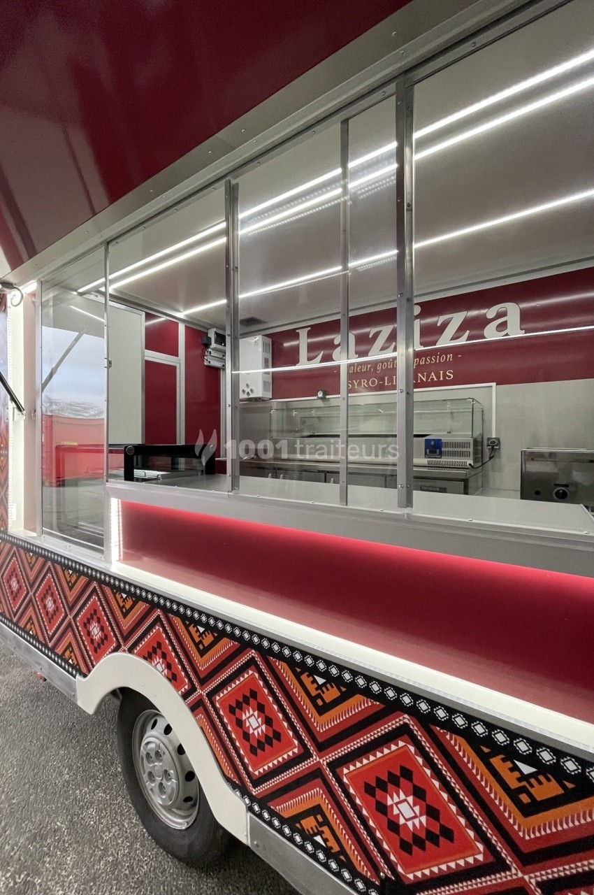 Camion de restauration rouge avec motifs géométriques, équipé d'une vitrine et d'un espace de préparation visible.
