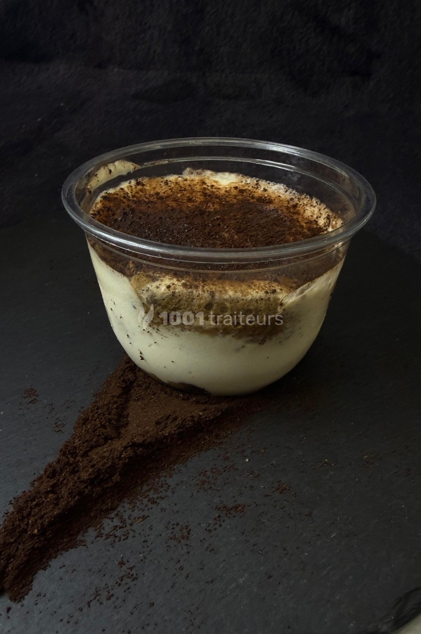 Dessert tiramisu en verrine, garni de cacao en poudre, posé sur une surface sombre avec du cacao renversé.