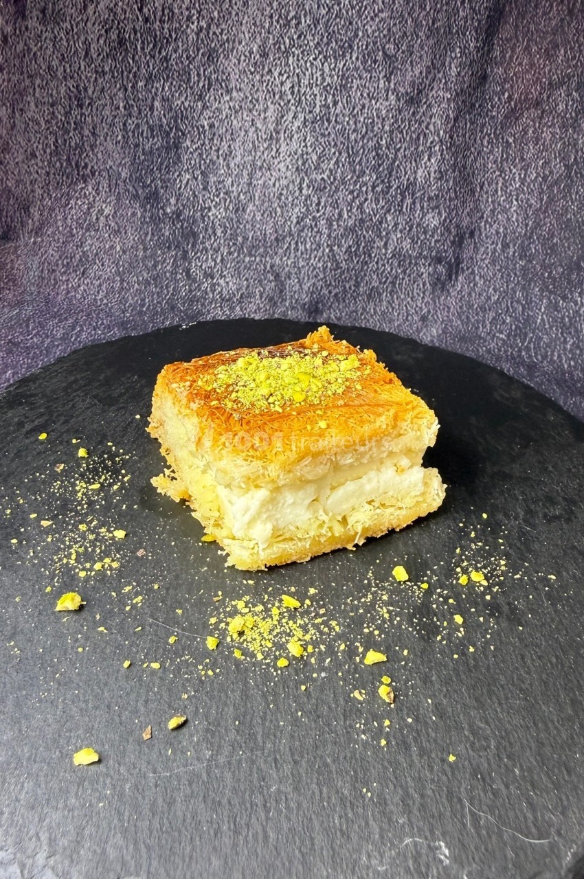 Part de dessert à base de pâte croustillante, garnie de crème et saupoudrée de pistaches, présentée sur une ardoise.