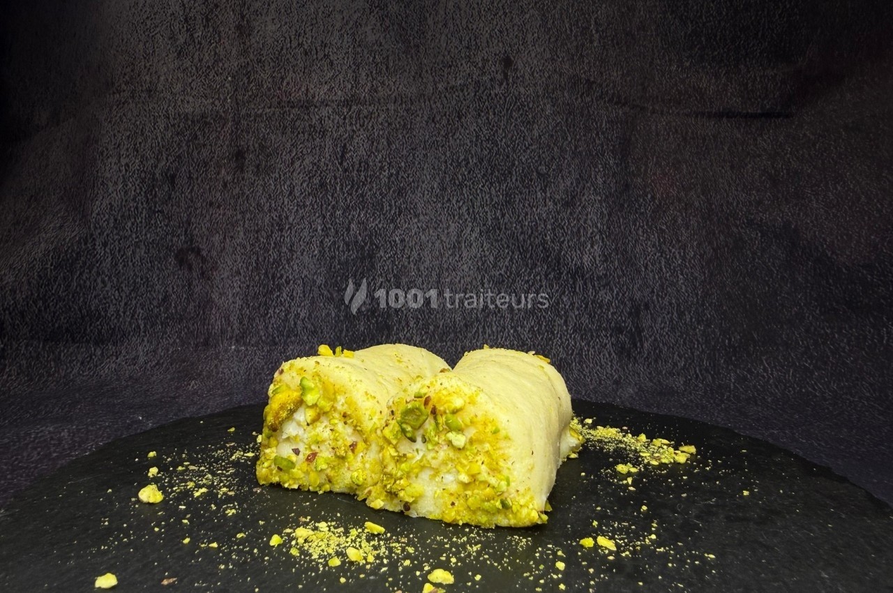 Deux morceaux de dessert à base de pistache, posés sur une surface noire avec un fond sombre.